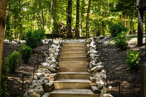 A wooden staircase surrounded by rocks and greenery, leading to a forested area. - Copper Ridge Hideaway - Dog Friendly | Pac Man Arcade Game | Hot Tub (Mineral Bluff)