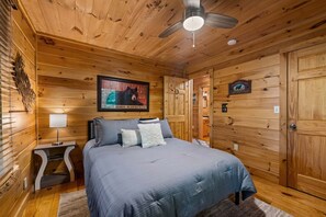 A wooden cabin bedroom with a bed, a nightstand, a ceiling fan, and a bear-themed poster. - Copper Ridge Hideaway - Dog Friendly | Pac Man Arcade Game | Hot Tub (Mineral Bluff)