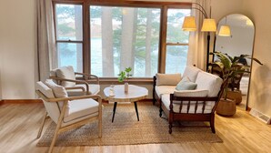 A room with a large window, wooden furniture, a round table, and a mirror. - Waterfront Paradise! Boat available for rent. (Waupaca)