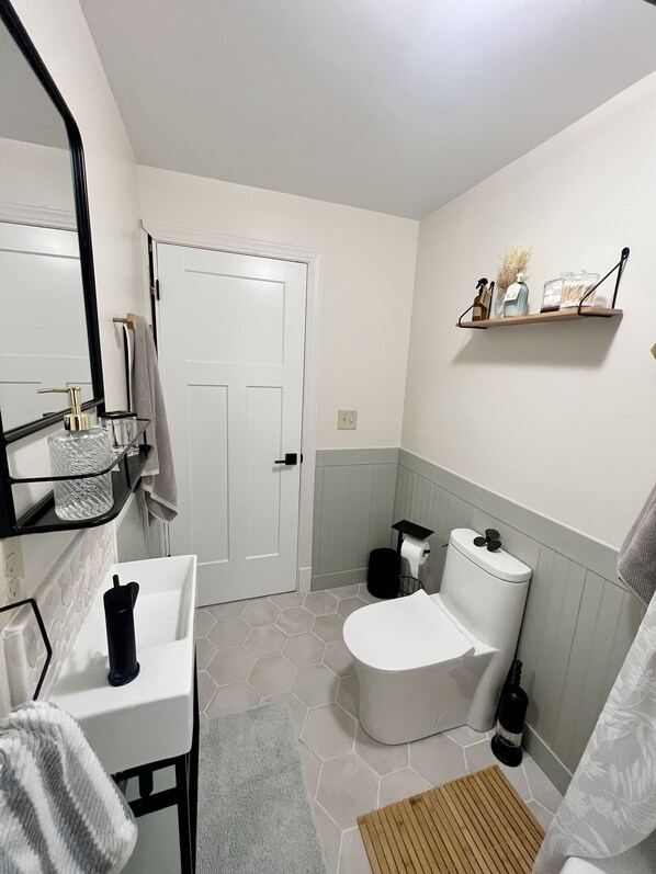 A bathroom with a white toilet, a sink with a mirror, and a shelf with toiletries. - Waterfront Paradise! Boat available for rent. (Waupaca)