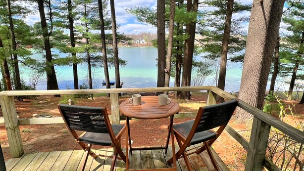A wooden deck with two chairs and a table, overlooking a lake surrounded by trees. - Waterfront Paradise! Boat available for rent. (Waupaca)