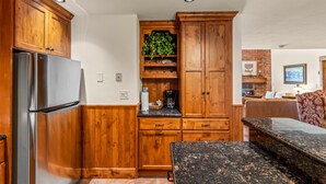 A kitchen with wooden cabinets, a stainless steel refrigerator, a countertop with a coffee maker, and a dining area with a bench. - Bear Claw 614 Premium On Mountain Condo with Ski-In/Ski-Out Access! (Steamboat Springs)