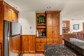 Une cuisine avec des meubles en bois, un réfrigérateur en acier inoxydable, un plan de travail avec une machine à café et un coin repas avec un banc.