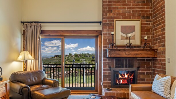 A living room with a fireplace, leather sofas, a view through a glass door, and a lamp. - Bear Claw 614 Premium On Mountain Condo with Ski-In/Ski-Out Access! (Steamboat Springs)