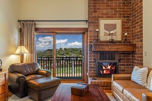 A living room with a fireplace, leather sofas, a view through a glass door, and a lamp. - Bear Claw 614 Premium On Mountain Condo with Ski-In/Ski-Out Access! (Steamboat Springs)