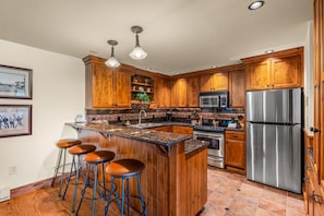 A kitchen with wooden cabinets, a stainless steel refrigerator, a microwave, a sink, and a bar stool area. - Bear Claw 614 Premium On Mountain Condo with Ski-In/Ski-Out Access! (Steamboat Springs)