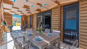 A wooden outdoor dining area with a table set for four, a hanging chair, and a grill. - Gorgeous home in Brodarica (Brodarica)