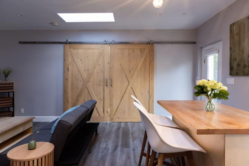 Een modern interieur met een houten schuifdeur, een eethoek met een houten tafel en stoelen, een bank en een kleine ronde tafel met een vaas.