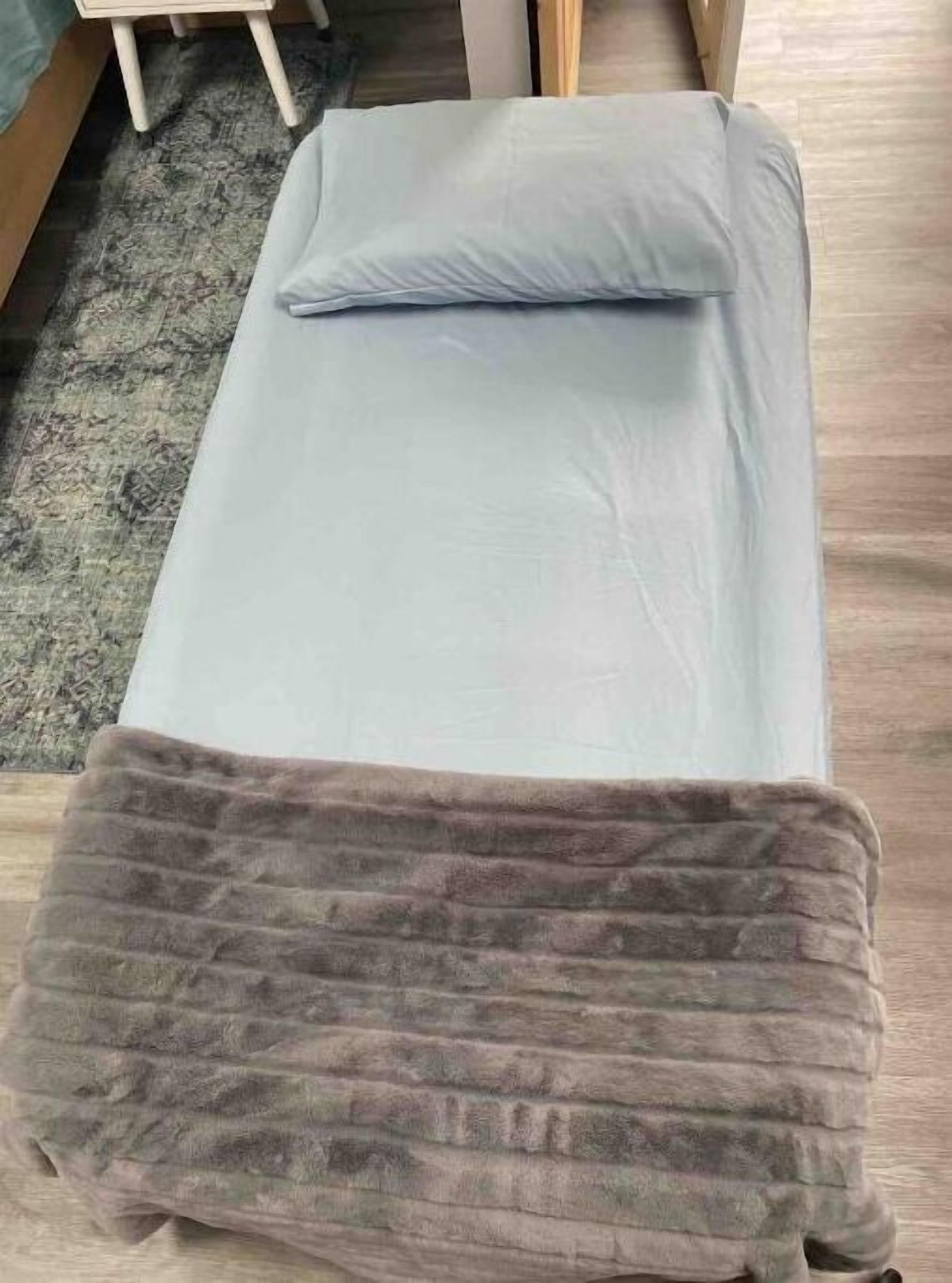 Ein kleines Bett mit grauem Lattenrost und einer braunen Decke.