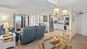 A living room with a sofa, a glass table with food, a lamp, and a view to the outside. - 🌴 Caprice Resort Unit #507 – Gulf Front Stunner with Full Kitchen & Balcony Views (Saint Pete Beach)