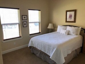 A bedroom with a large bed, two windows with blinds, a bedside lamp, and a framed picture on the wall. - C24 home by pool & Gorge shuttle (Quincy)