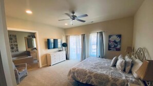 A bedroom with a bed, a dresser, a vanity with a mirror, a ceiling fan, and a painting on the wall.