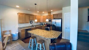 A modern kitchen with wooden cabinets, a granite countertop, stainless steel appliances, and two bar stools.