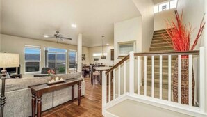A spacious living area with a wooden floor, a sofa, a dining table, and a staircase with a railing.