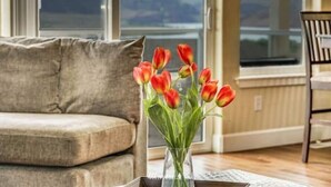 A living room with a beige sofa, a glass vase with red tulips, and a view of a mountain through large windows.