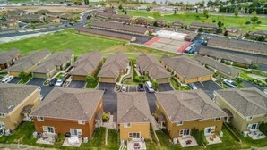 A residential area with multiple two-story houses, a central sports field, and a lake in the background.