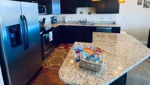 A modern kitchen with dark cabinets, stainless steel appliances, a granite countertop island, and pendant lighting. - D28-ATCH Garage 2 Decks/Patio Sunserra Gorge AMP (Quincy)