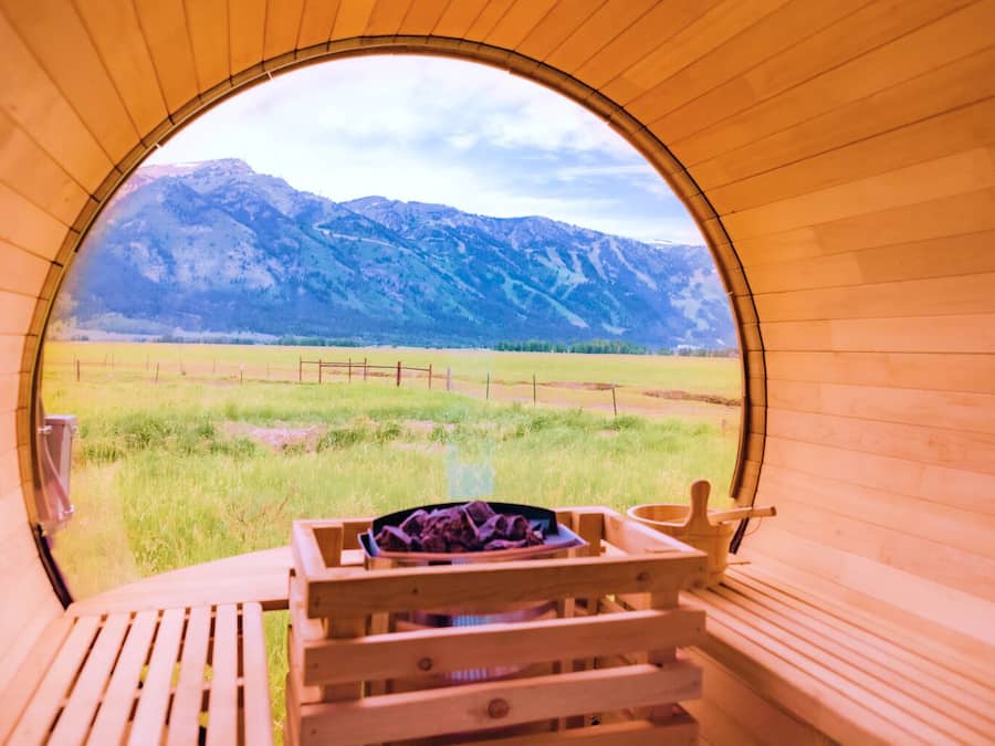 Una sauna de madera con un ventanal circular, un banco de madera y una pequeña mesa con una toalla.