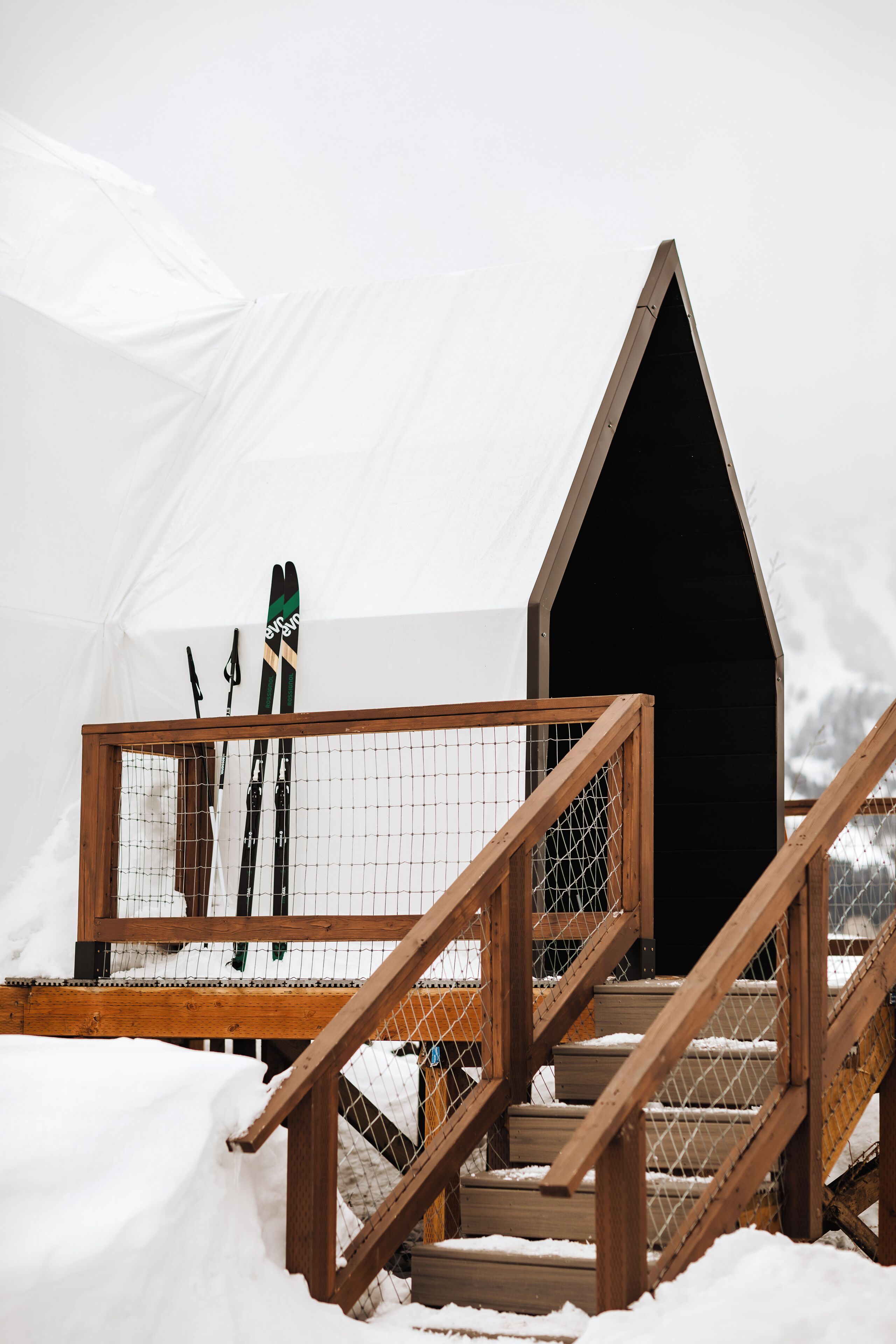 Un escalier en bois mène à un bâtiment dont le toit est noir, avec une tente blanche en arrière-plan.