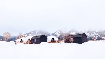 A snow-covered landscape with three barns and a mountain in the background.