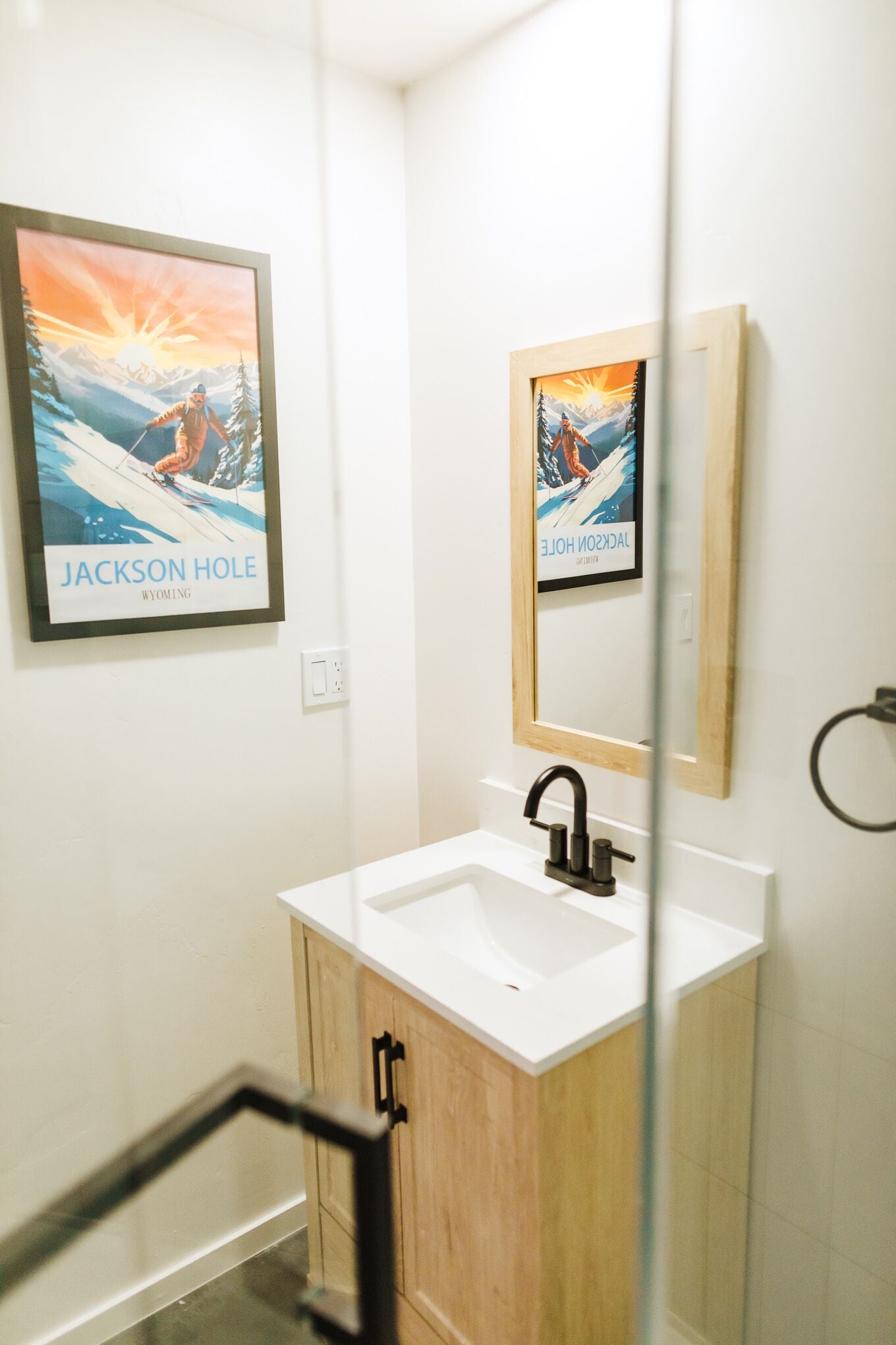 A bathroom with a white sink, wooden cabinets, a black faucet, and two framed pictures of Jackson Hole, Wyoming.