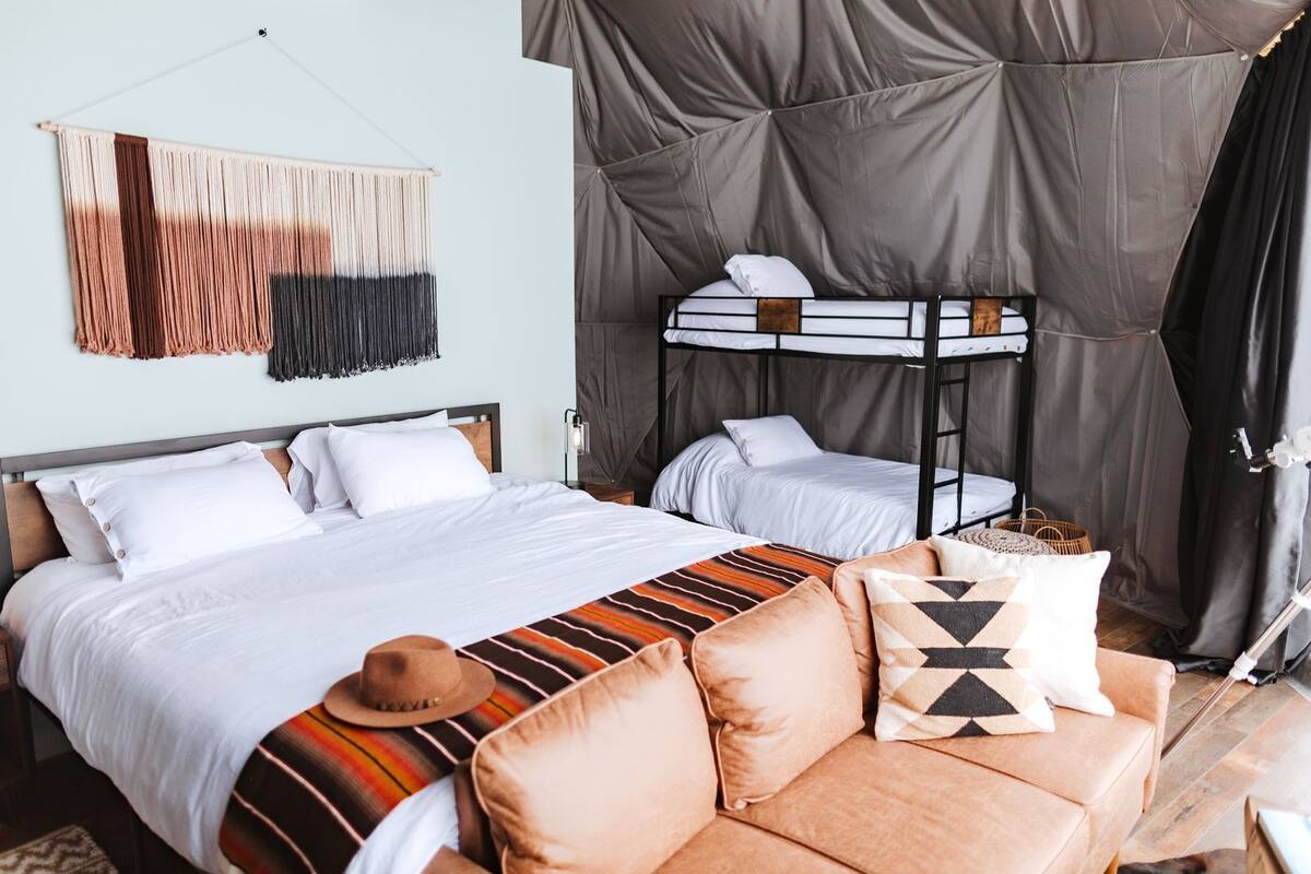 A room with a bunk bed, a sofa, a patterned blanket, and a wall hanging.