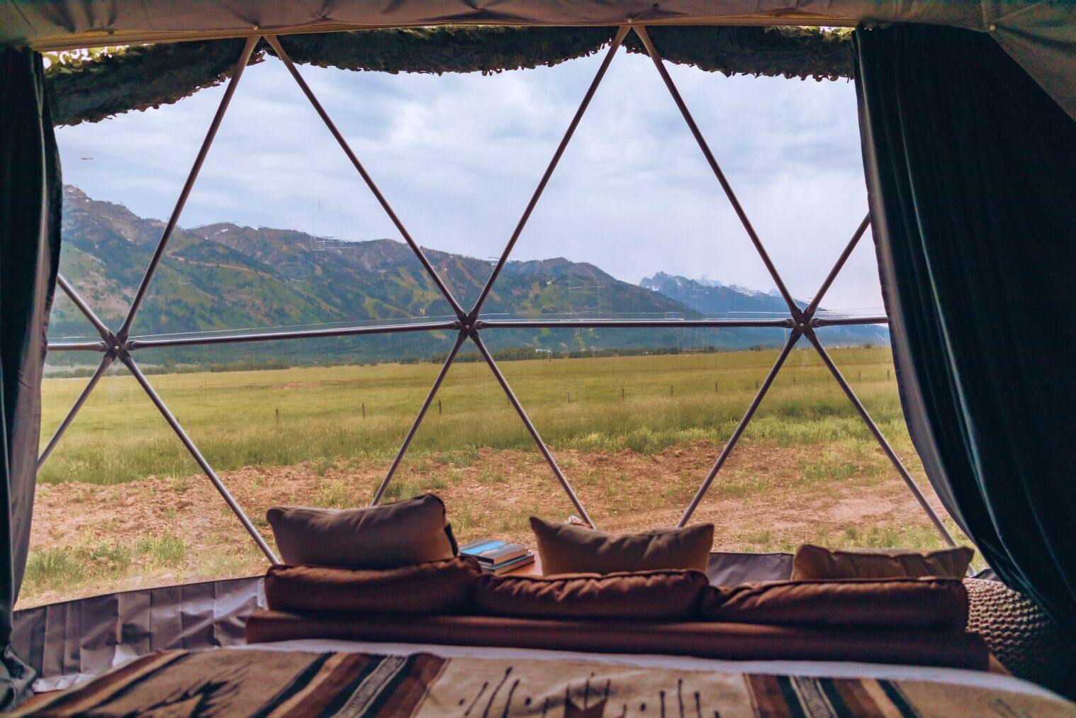 Uma tenda com vista para um campo gramado e montanhas.