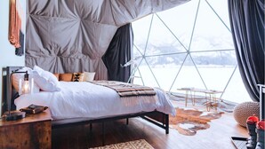 A cozy bedroom with a large window, a wooden bedside table, and a bed with a patterned blanket. - Tammah Jackson Hole (Wilson)