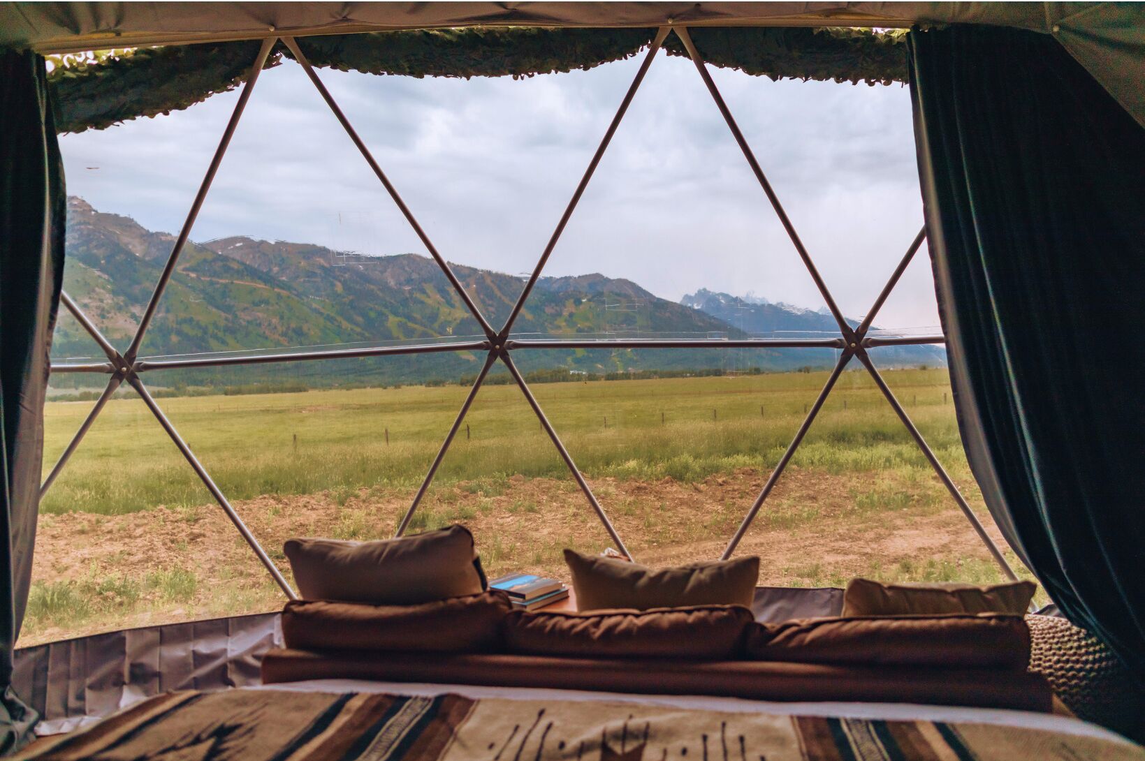 A tent with a view of a grassy field and mountains.