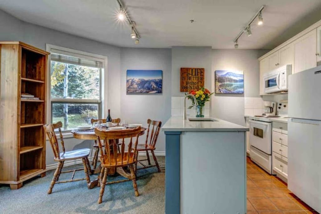 A modern kitchen with white cabinets, a central island, and a dining area with wooden chairs and a table.