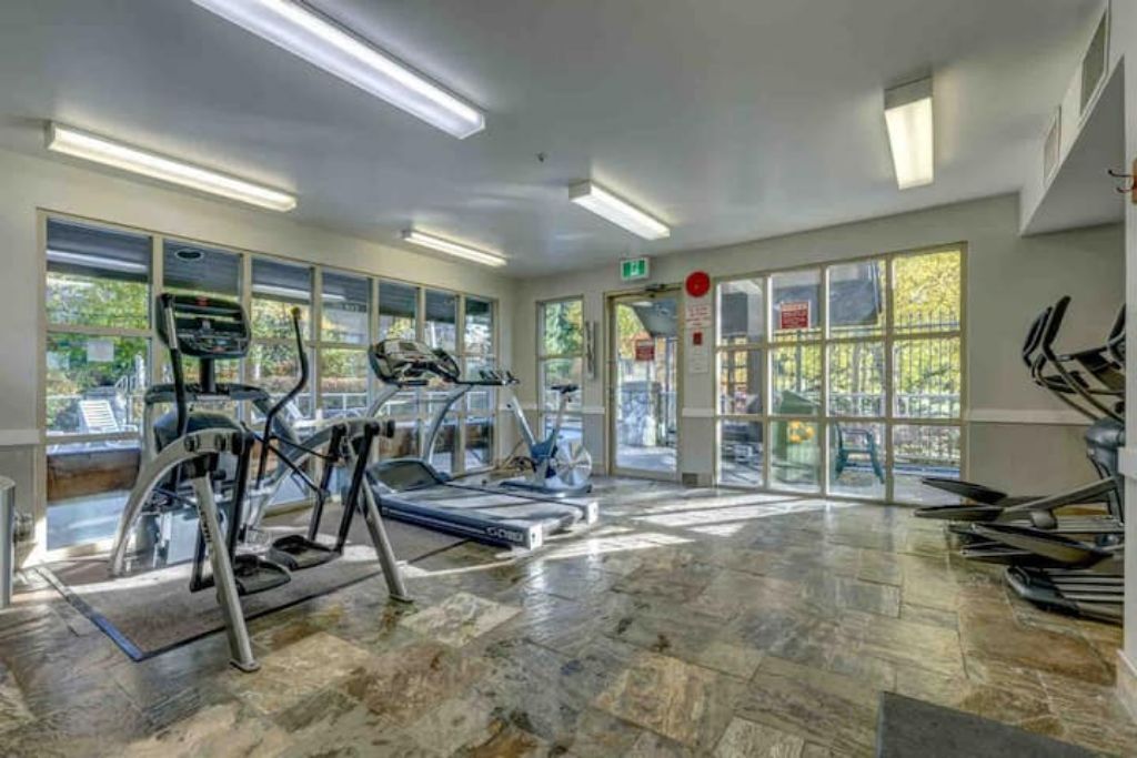 Een fitnessruimte met loopbanden, hometrainers en een spiegelwand.