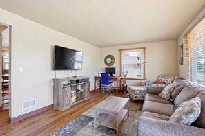A living room with a TV, wooden cabinet, blue office chair, and a patterned sofa. - Cozy Home with HOT TUB (Kimberly)