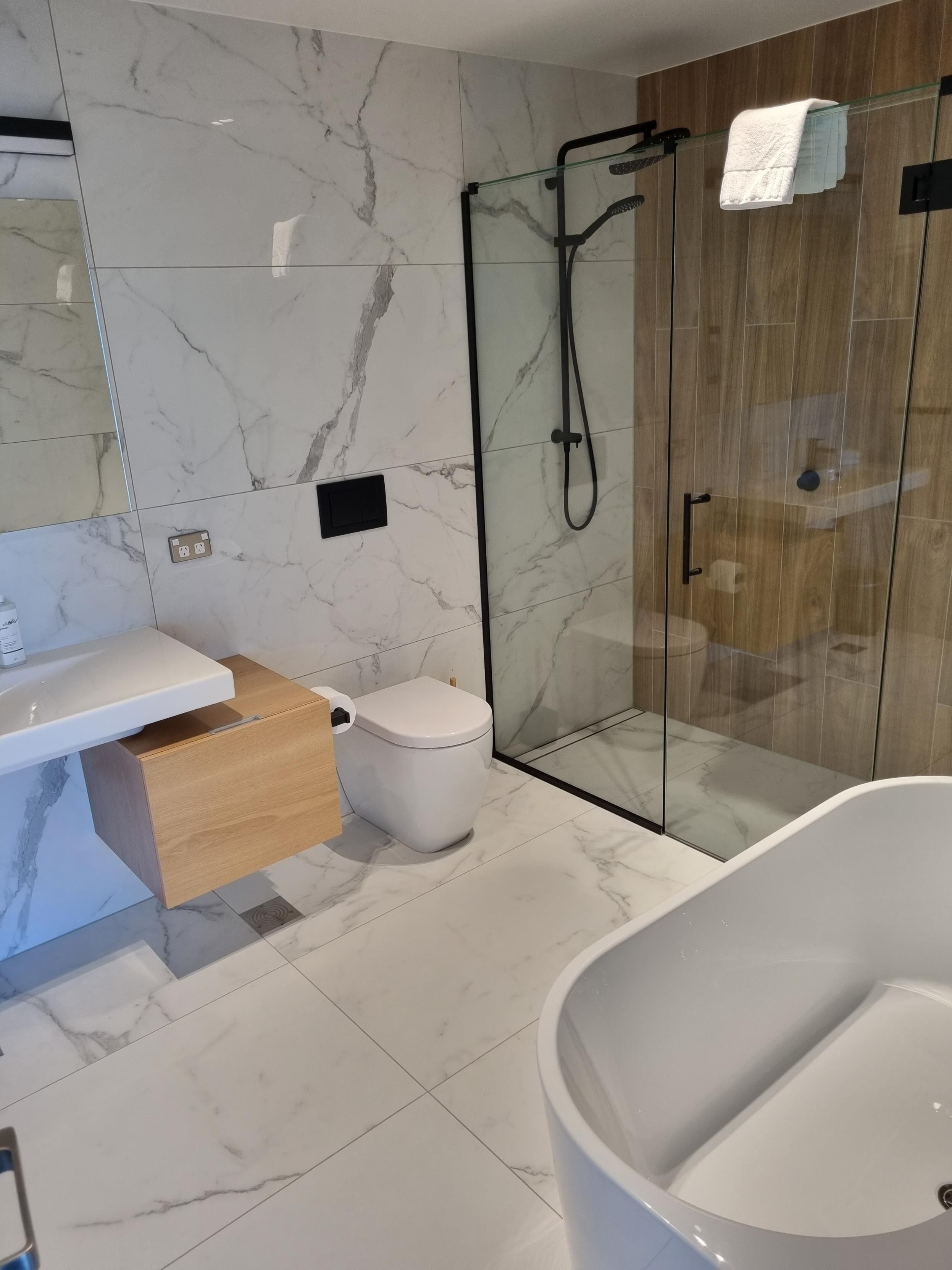 A modern bathroom with a marble-tiled floor, a white toilet, a glass-enclosed shower, and a freestanding bathtub.