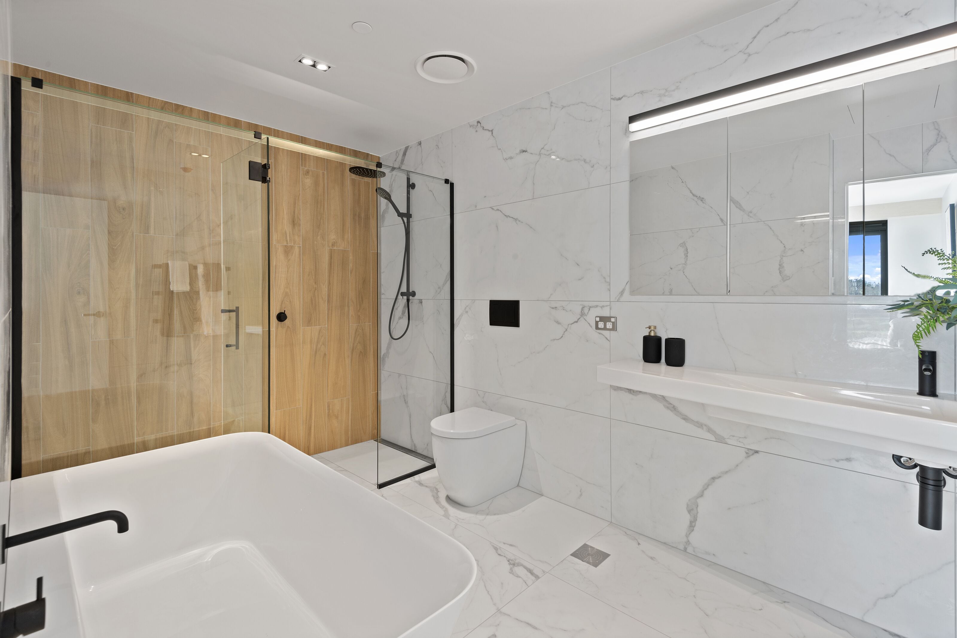 Un bagno moderno con cabina doccia in vetro, una vasca da bagno bianca, un water e una parete rivestita in marmo.