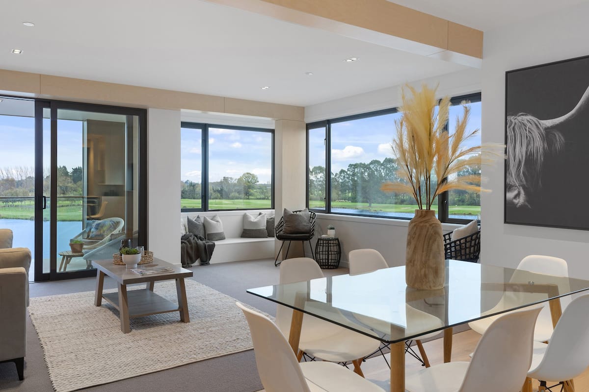A spacious living area with a glass dining table, comfortable seating, and large windows offering a view of the outdoors.