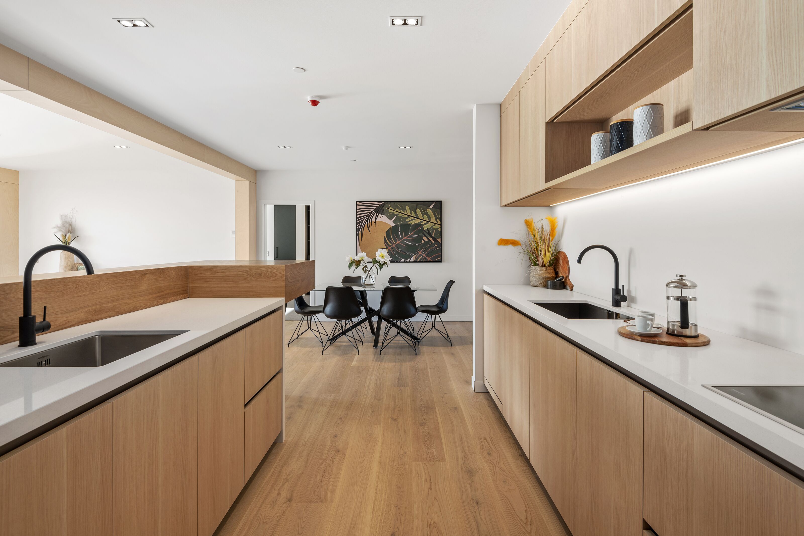 A modern kitchen with wooden cabinets, black chairs, a dining table, and a coffee maker on the counter.