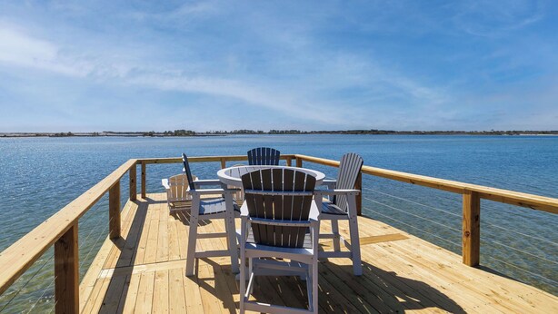 Une terrasse en bois, avec des chaises et une table, donnant sur une étendue d’eau.