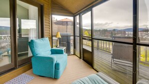 Ein überdachter Balkon mit blauem Stuhl, einem kleinen Tisch mit Lampe und Blick auf eine Terrasse und Berge.