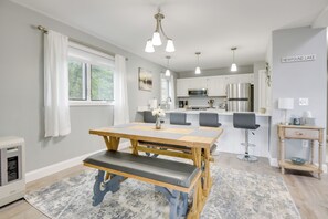 A modern kitchen with white cabinets, stainless steel appliances, and a wooden dining table with a bench.