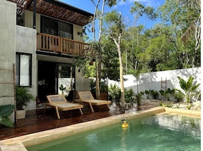 Una casa moderna con piscina, terraza de madera y plantas tropicales.