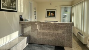 A modern hotel lobby with a marble reception desk, framed pictures on the walls, and a large window with blinds. - The Hamlet Inn at Warwick (Warwick)