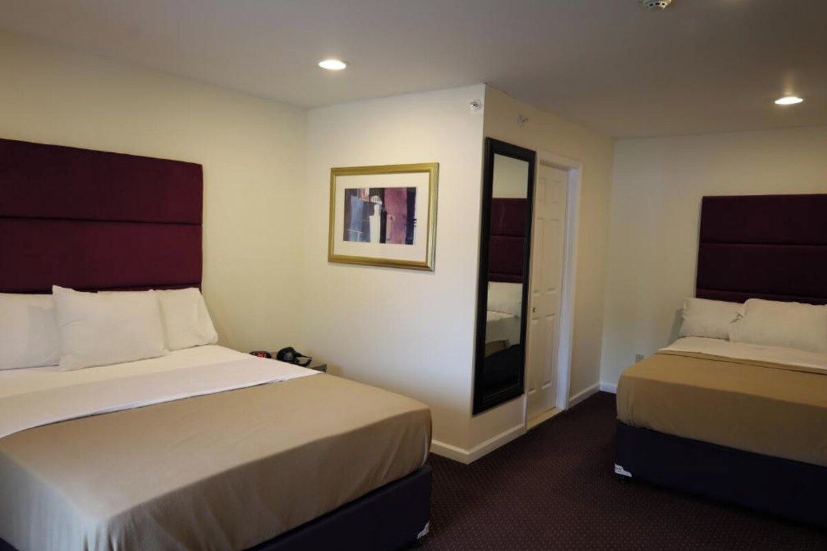 A hotel room with two beds, a door, a framed picture on the wall, and a carpeted floor.