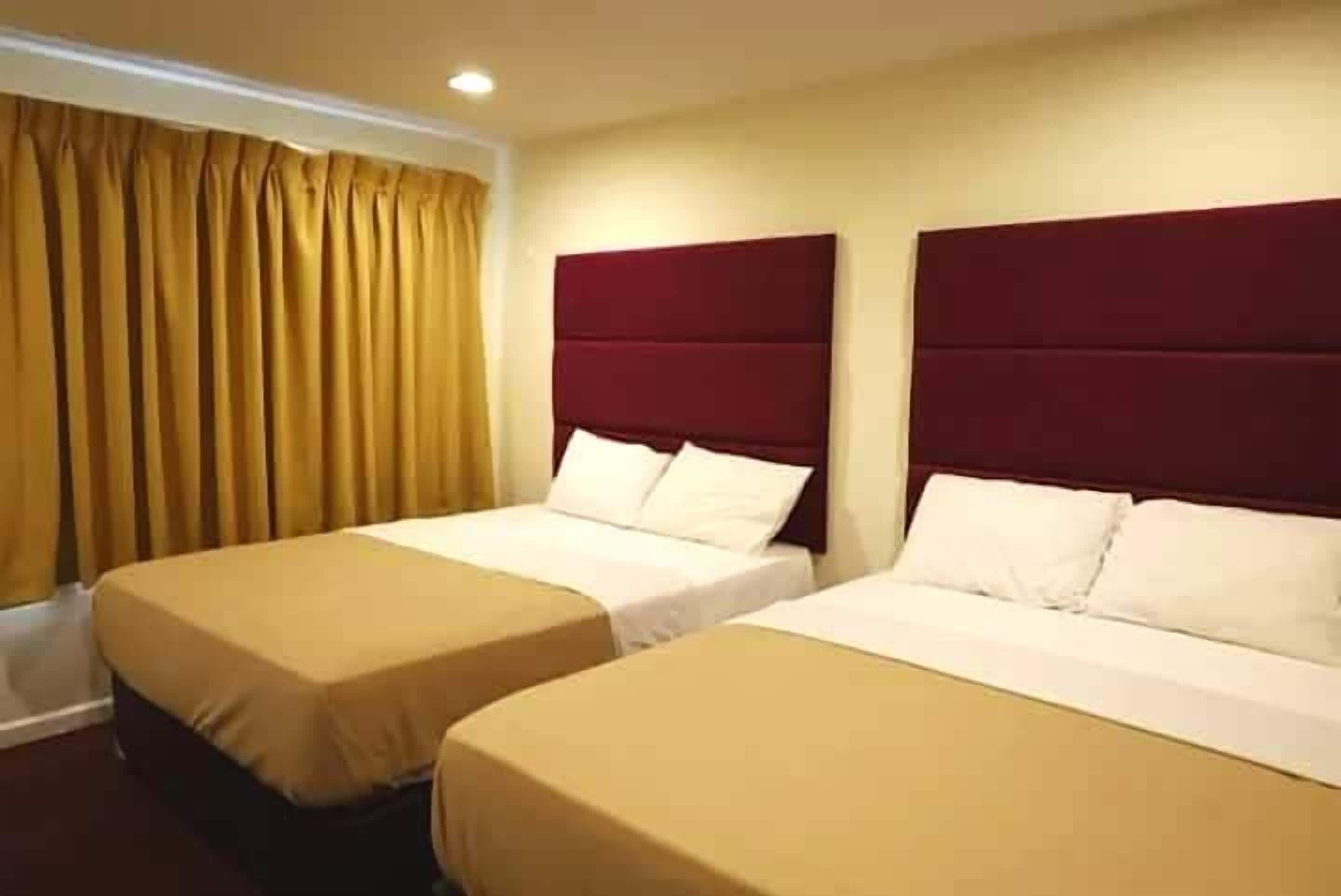 A hotel room with two beds, a window with curtains, and a red headboard.