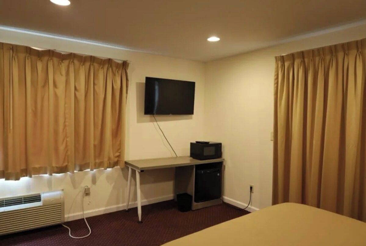 Ein Hotelzimmer mit einem Bett, einem Schreibtisch mit Fernseher und Vorhängen.