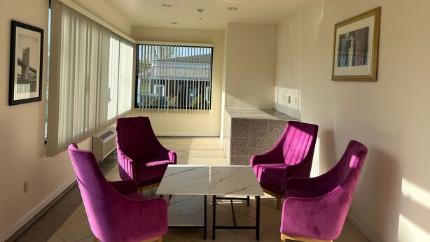 A modern room with a marble table and four purple chairs, a large window with blinds, and a framed picture on the wall. - The Hamlet Inn at Warwick (Warwick)