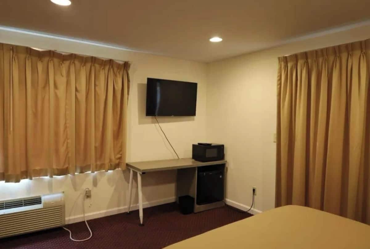 A hotel room with a bed, a desk with a television, and curtains.