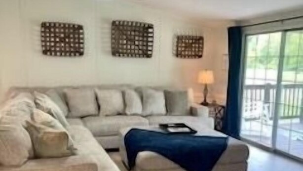 Una sala de estar con sofá, reposapiés, ventilador de techo y ventanas amplias.