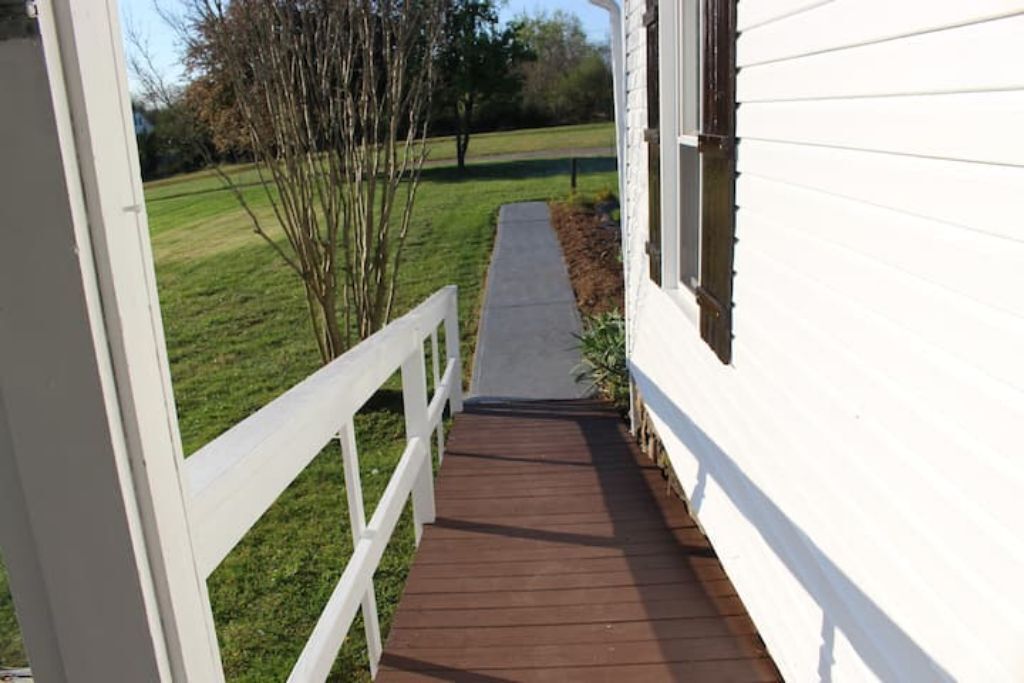 Une terrasse en bois mène à un bâtiment blanc doté d’une balustrade blanche.