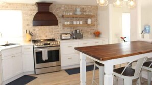 Una cocina moderna con armarios blancos, una isla de madera y lámparas colgantes.