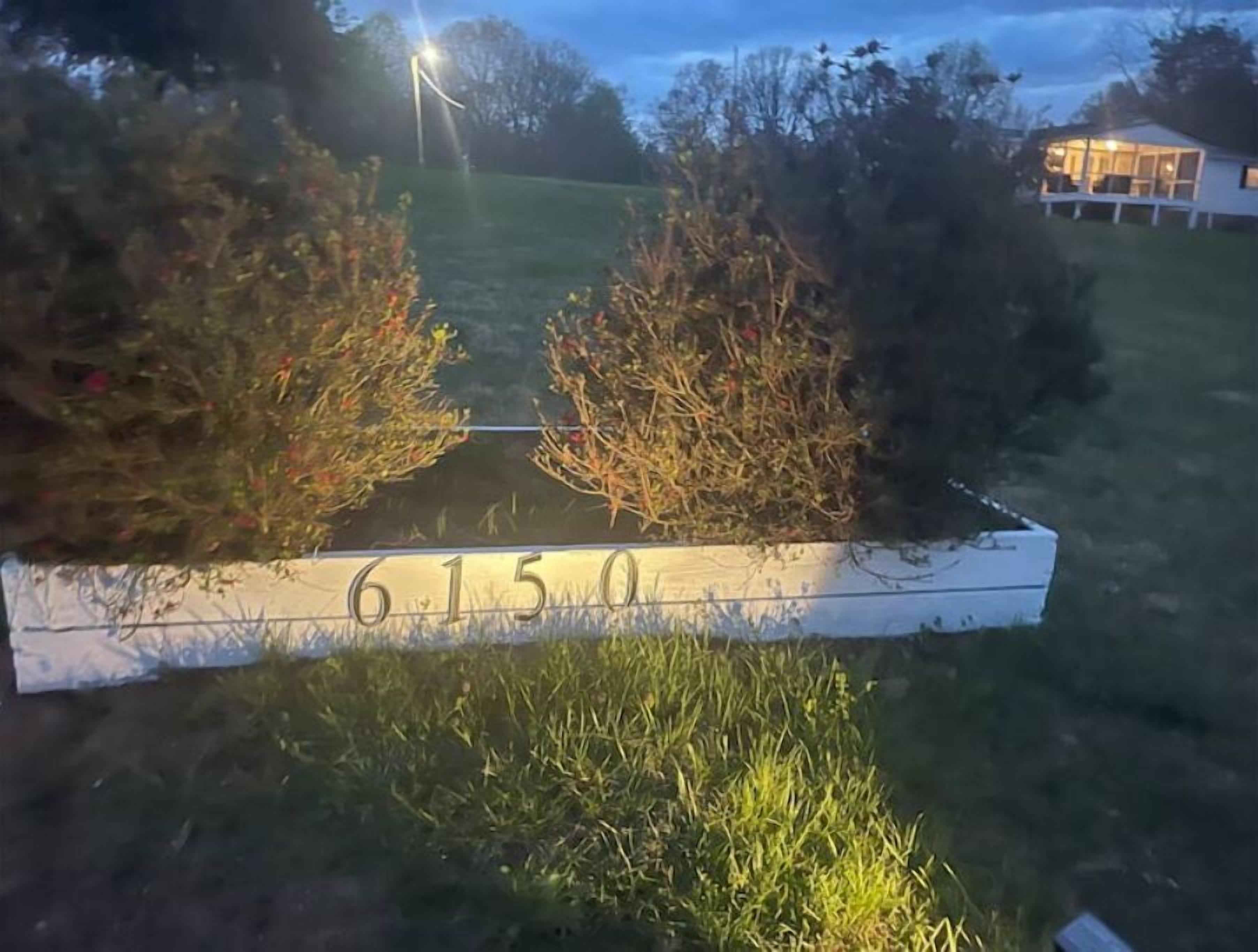 A white sign with the number 6150 in a grassy area with bushes.